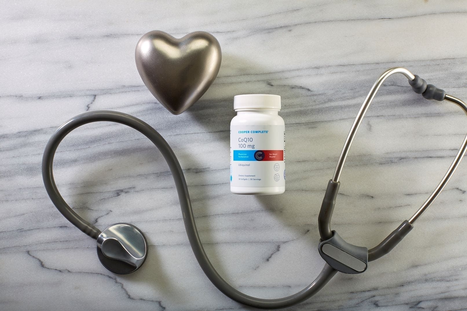 Cooper Complete CoQ10 50mg Ubiquinol dietary supplement bottle on a marble surface with stethoscope and metal heart shaped object