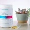 Cooper Complete Healthy Body Daily Vitamin Pack dietary supplement canister and a single daily packet on a counter with several succulent plants