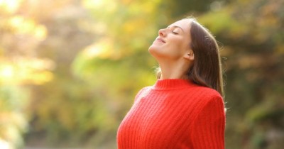 Photo of a younger woman outdoors in a red sweater breathing deeply, depicting melatonin benefits for mood, stress and anxiety