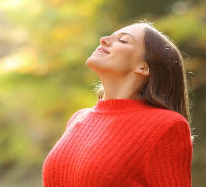 Photo of a younger woman outdoors in a red sweater breathing deeply, depicting melatonin benefits for mood, stress and anxiety