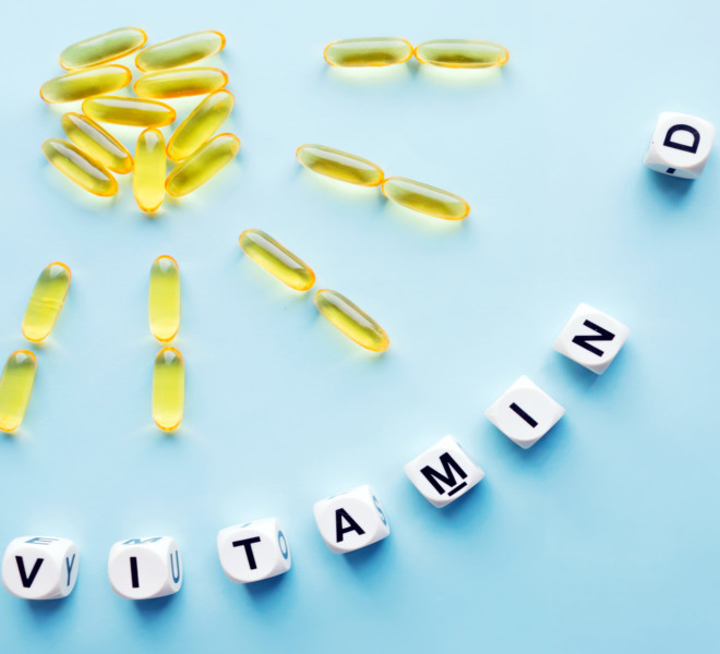 Photo of yellow softgels arranged as a sun and the word Vitamin D spelled out in baby letters