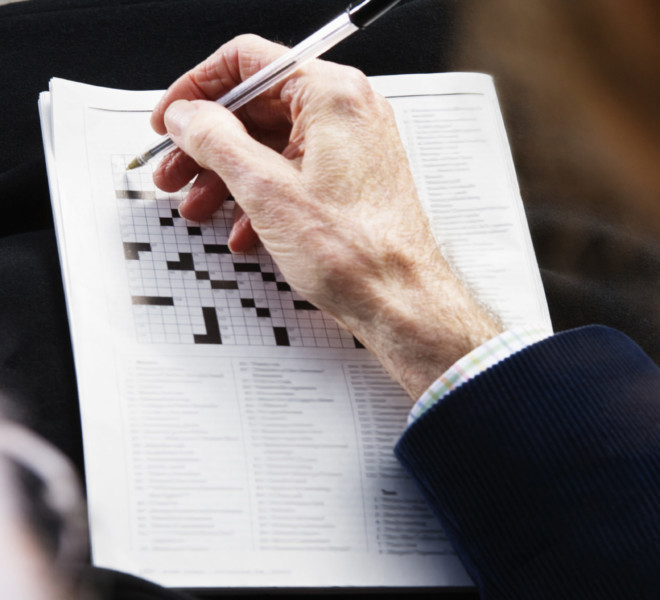 Close up of senior man's hand with pen on crossword puzzle