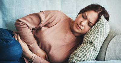 Image of a young woman resting uncomfortably on a sofa and clutching her stomach.