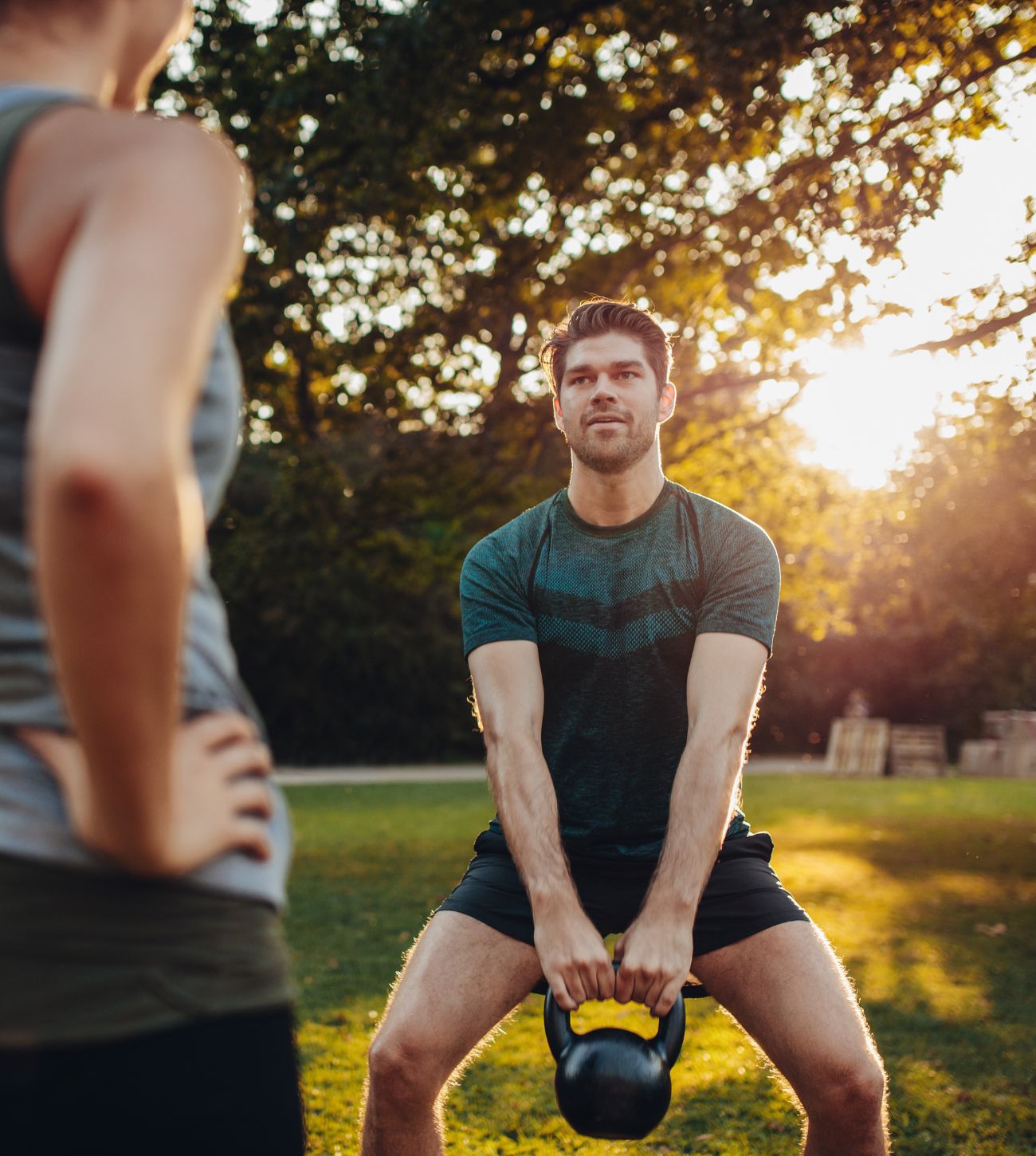 Photo of an athletic man outdoors doing a kettle bell routine.