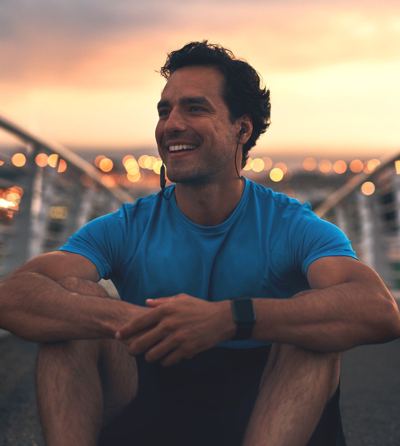 Photo of a smiling man relaxing on a bridge after a workout.