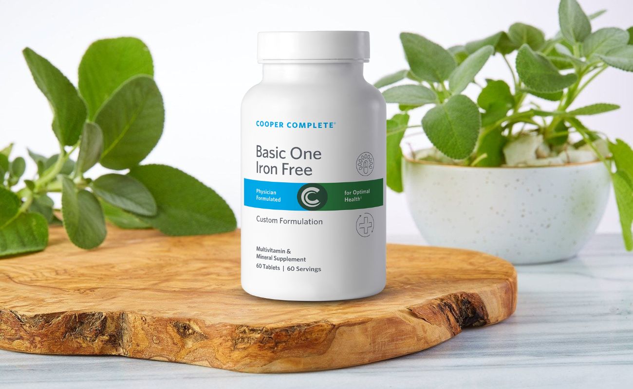 Photo of Cooper Complete Basic One Daily Multivitamin Iron Free bottle on a wood and marble surface with greenery.
