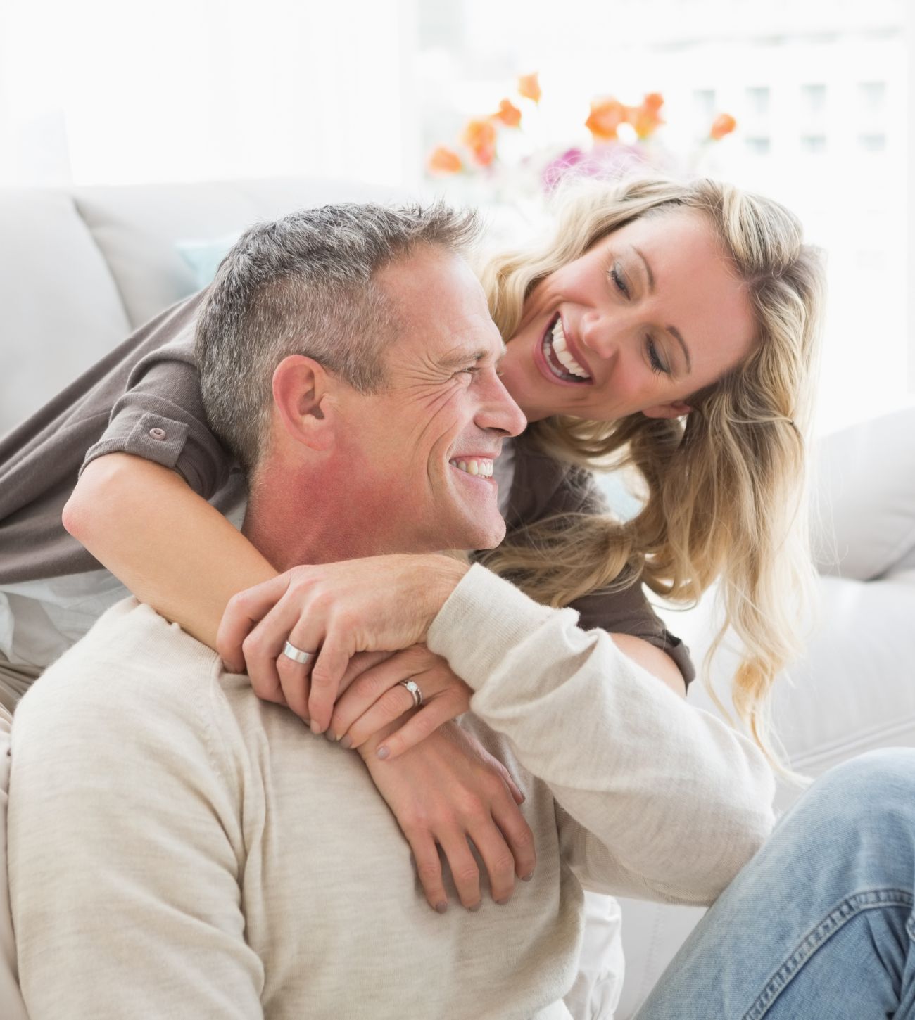 Photo of an adult couple smiling and hugging as they enjoy time together at home on the sofa and floor.