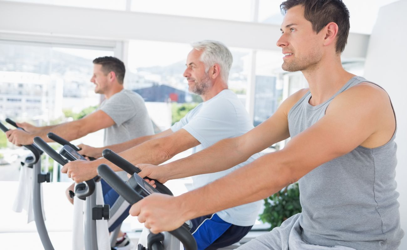 Photo of three adult men of various ages on spin bikes taking a class together.