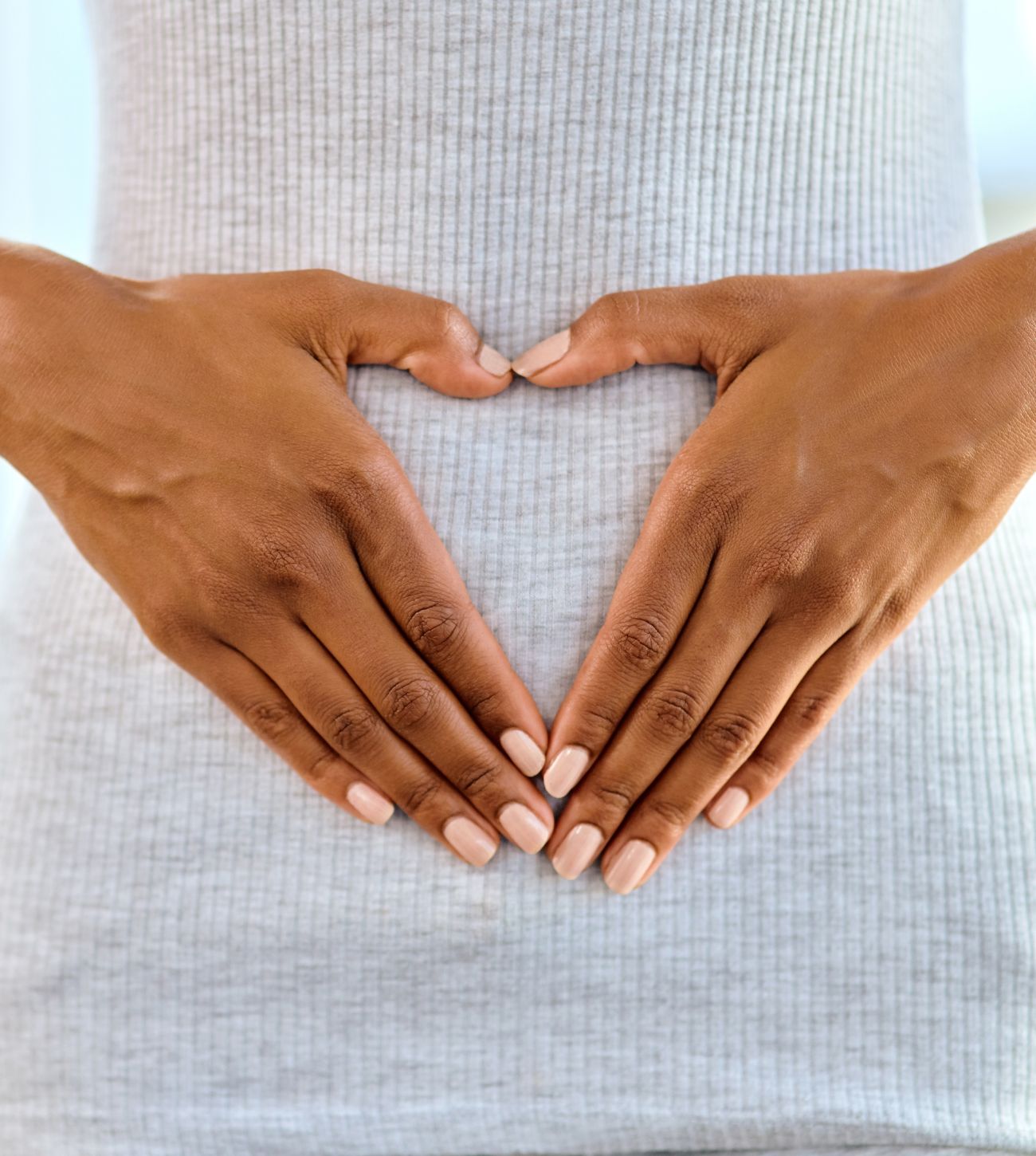 Photo of a young woman's hands in heart position on top of her stomach or gut.