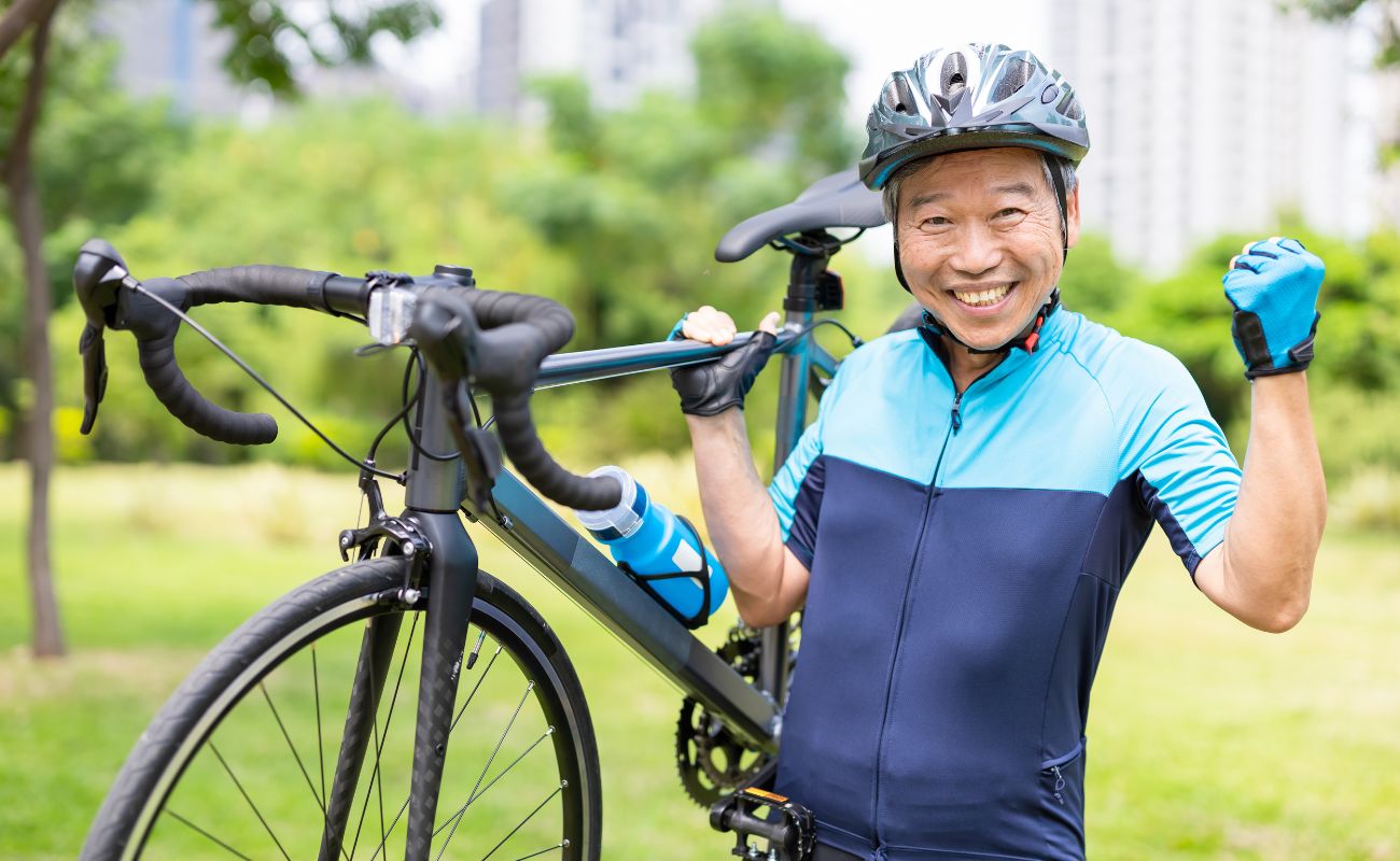 Photo of an older man in his cycling gear lifting his bicycle and flexing his arm muscles.