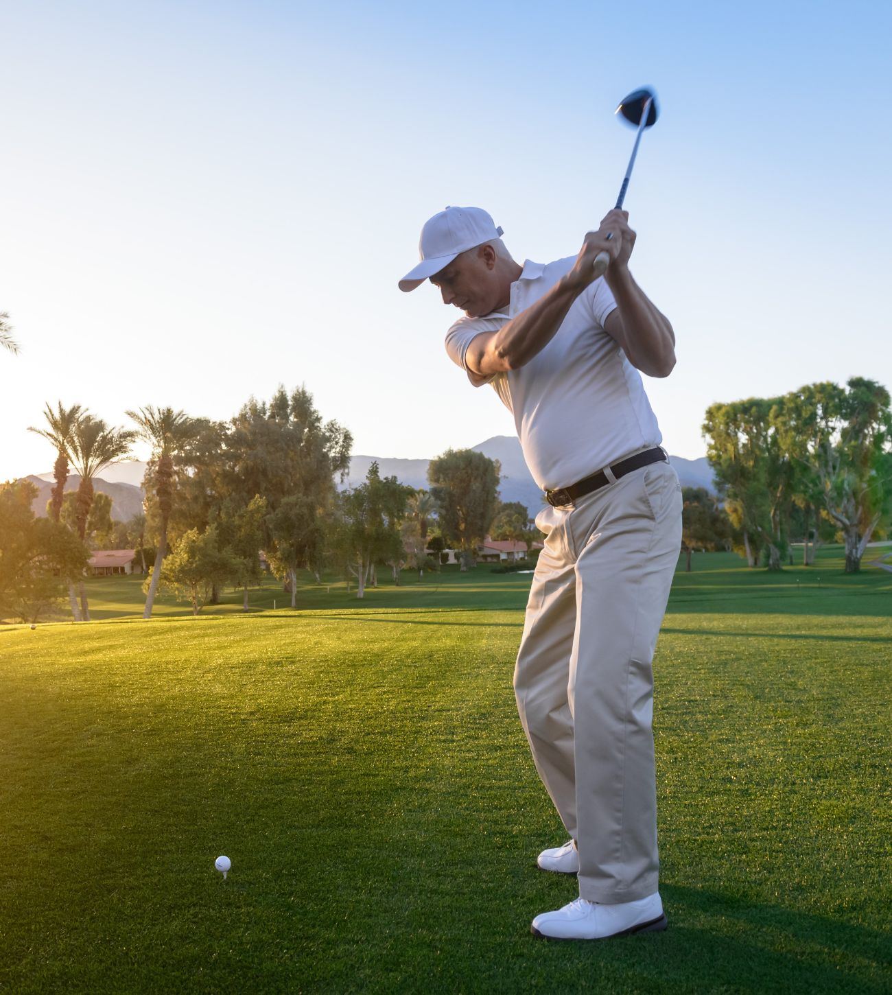 Photo of a man on a golf course on a sunny morning, about to hit the ball from the tee.