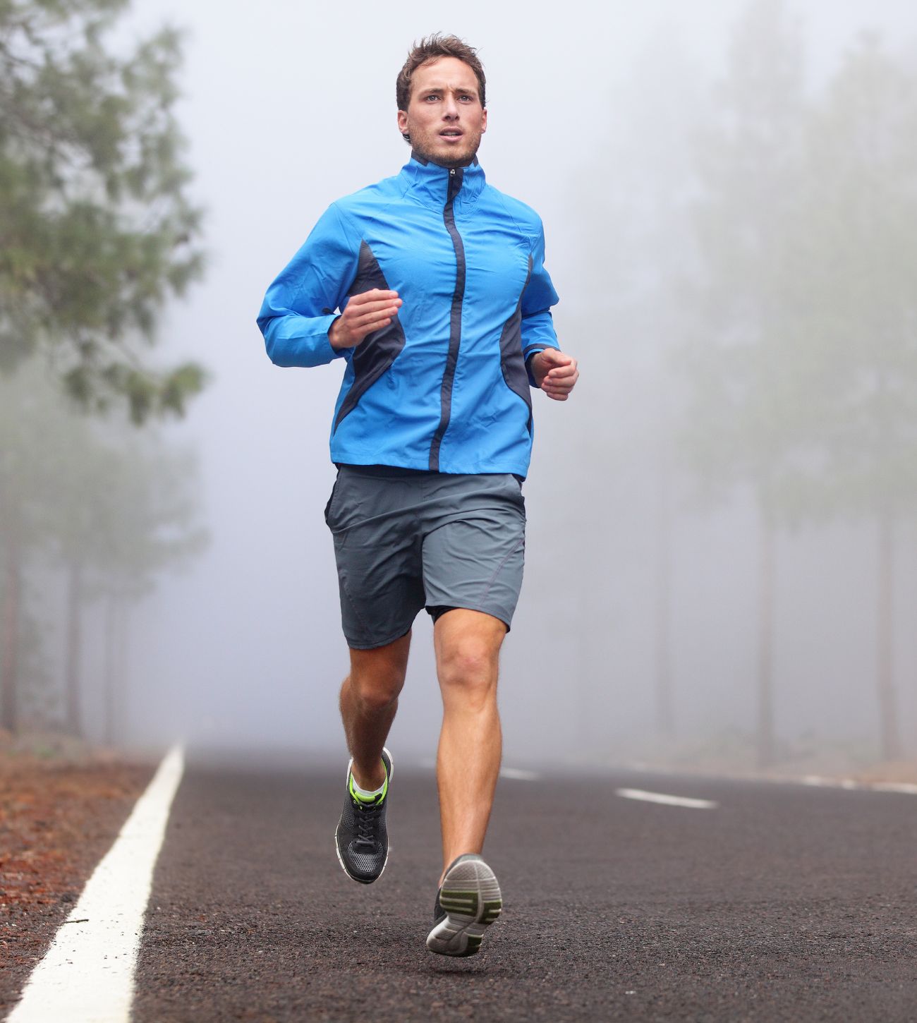 Photo of a man jogging on the road on a cooler, foggy morning.