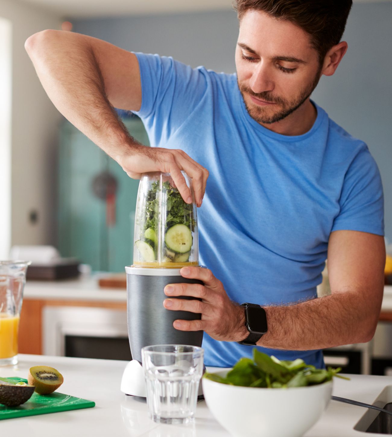 Photo of a man in the kitchen blending together a green smoothie.