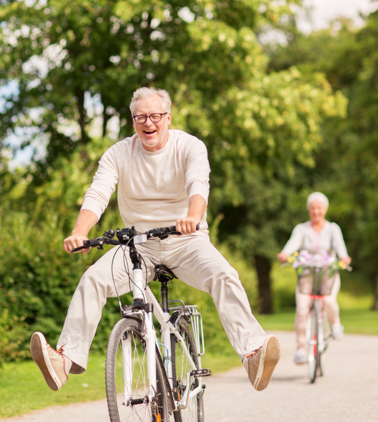 Photo of a man and woman riding old-school bikes on a wide park path.