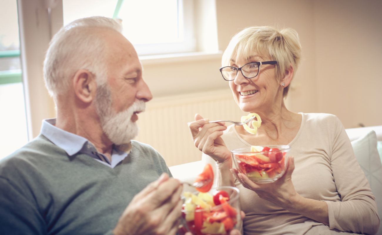 Photo of a mature couple relaxing on the sofa and each holding and enjoying a healthy meal in a glass bowl.