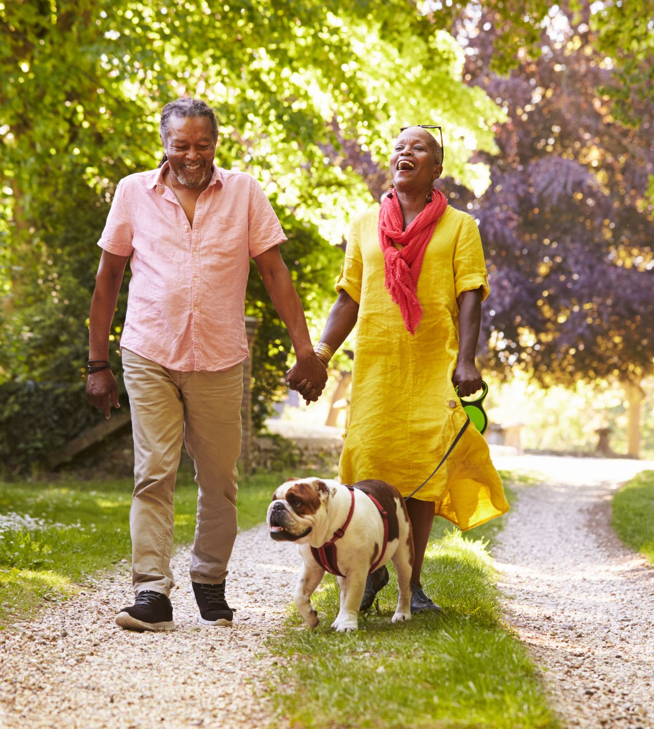 Photo of a mature African American couple enjoying a walk outdoors with their pet bulldog.