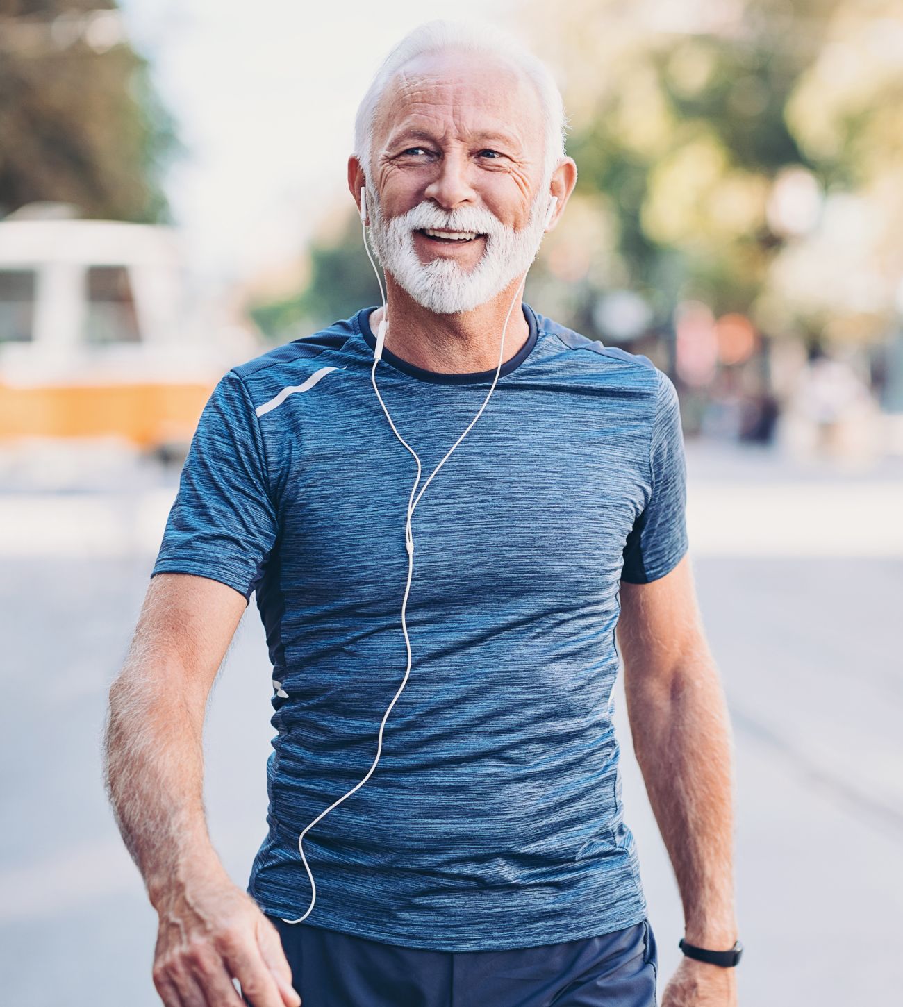 Photo of a mature fit man walking while listening to a podcast or music on wired headphones.