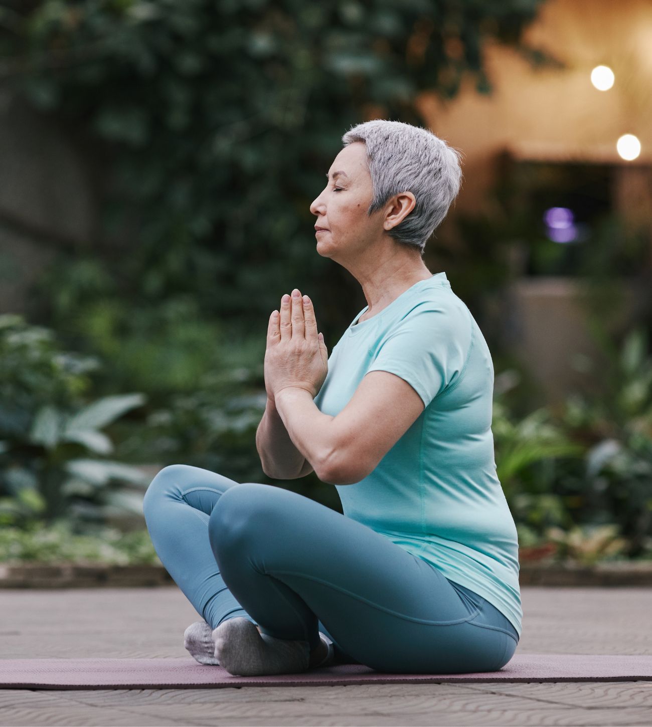 Photo of a mature woman sitting cross-legged on the ground and meditating outdoors