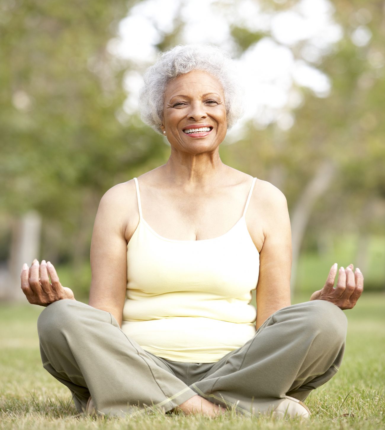 Photo of a mature woman sitting cross-legged on the ground and meditating outdoors