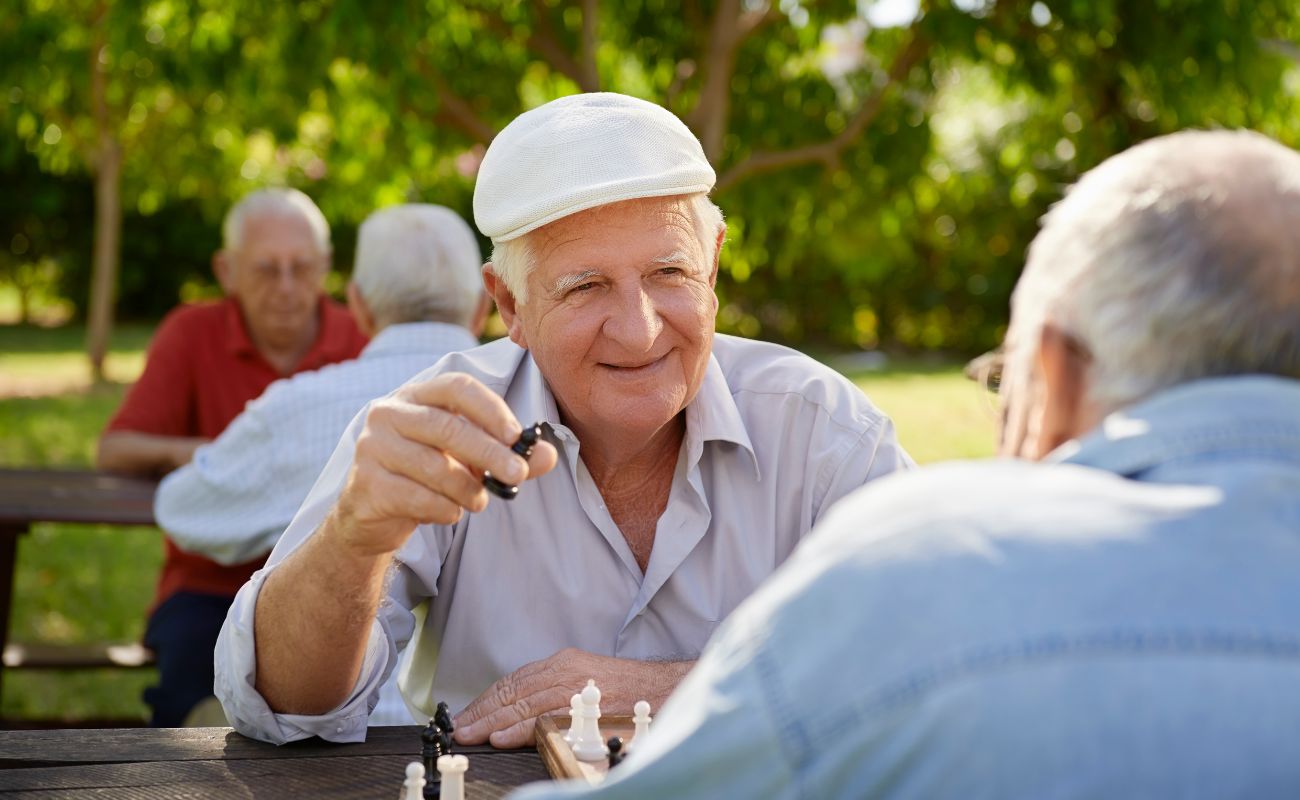 Photo of four retired men playing chess outdoors in the park.