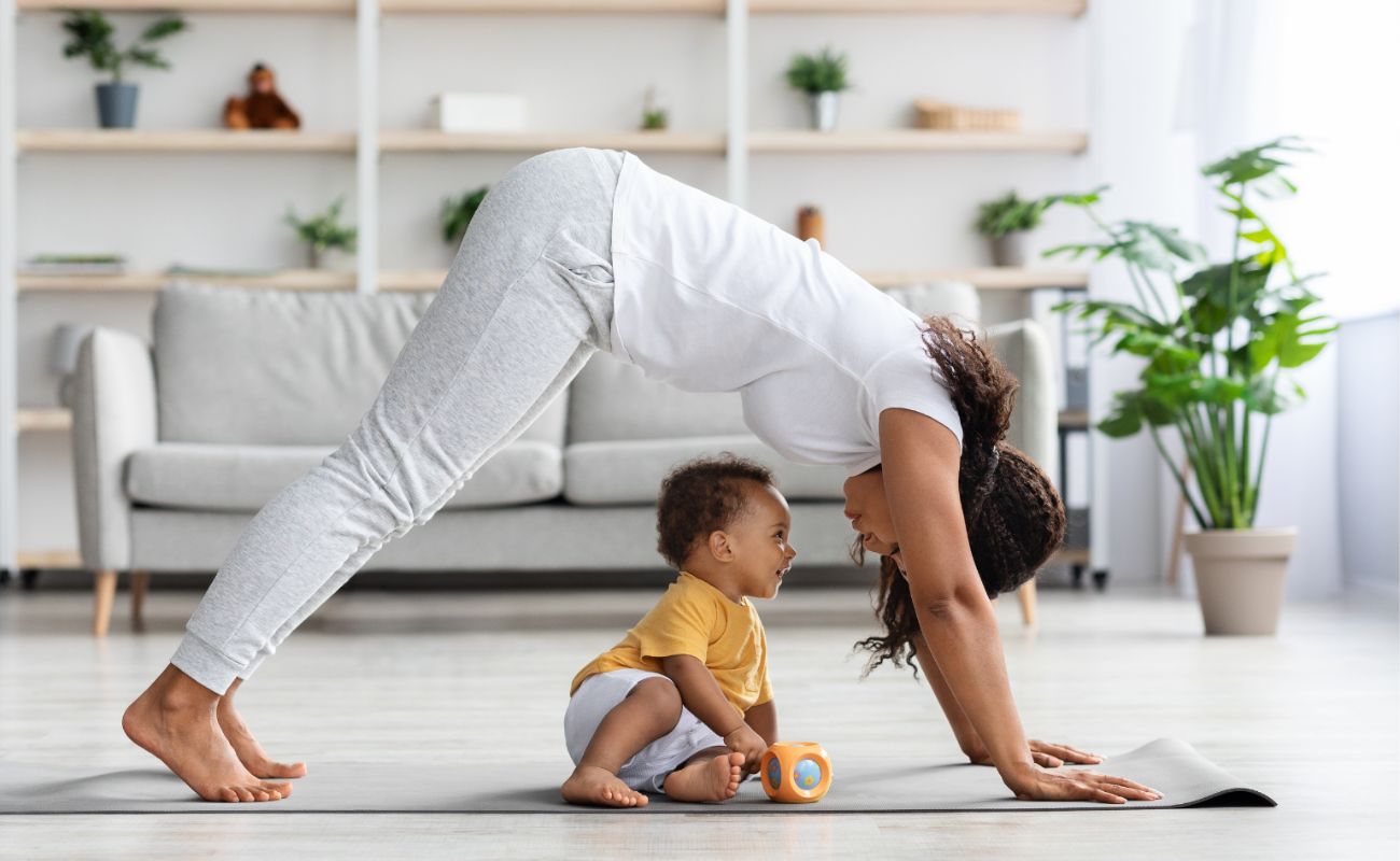 Photo of a young mother in a yoga pose with her infant child beneath her on the yoga mat.