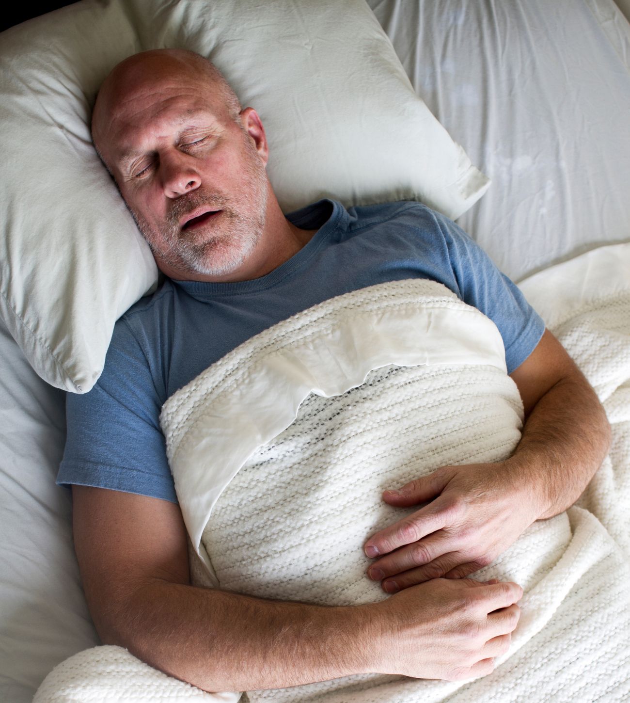 Photo of a man sleeping in bed with his mouth open.