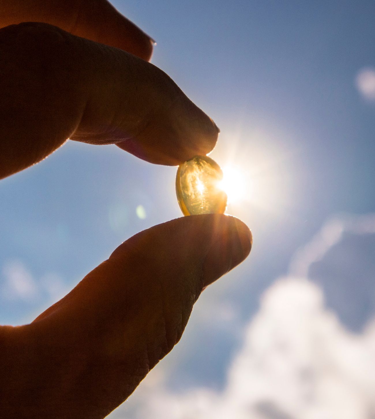 Photo of a vitamin D3 capsule being held in a hand against the sun.