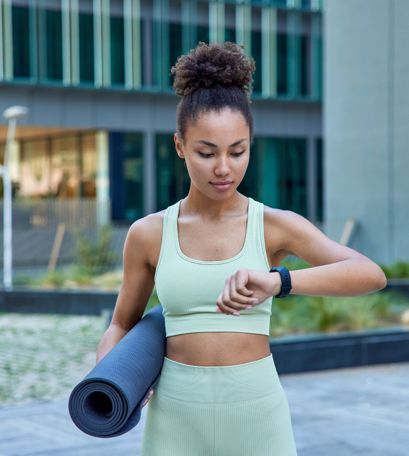 Young woman holding a yoga mat and looking at her watch.
