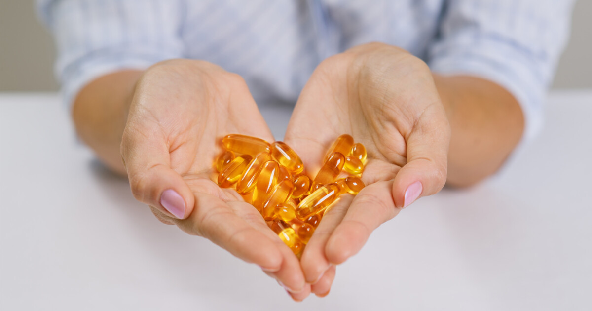 Feminine, manicured hands cupped in a heart shape and holding what looks like a bunch of omega-3 softgels